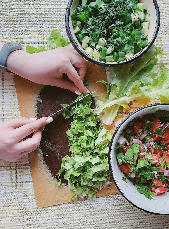 Hands chopping fresh vegetables for salad on a wooden board. Vibrant and healthy ingredients.