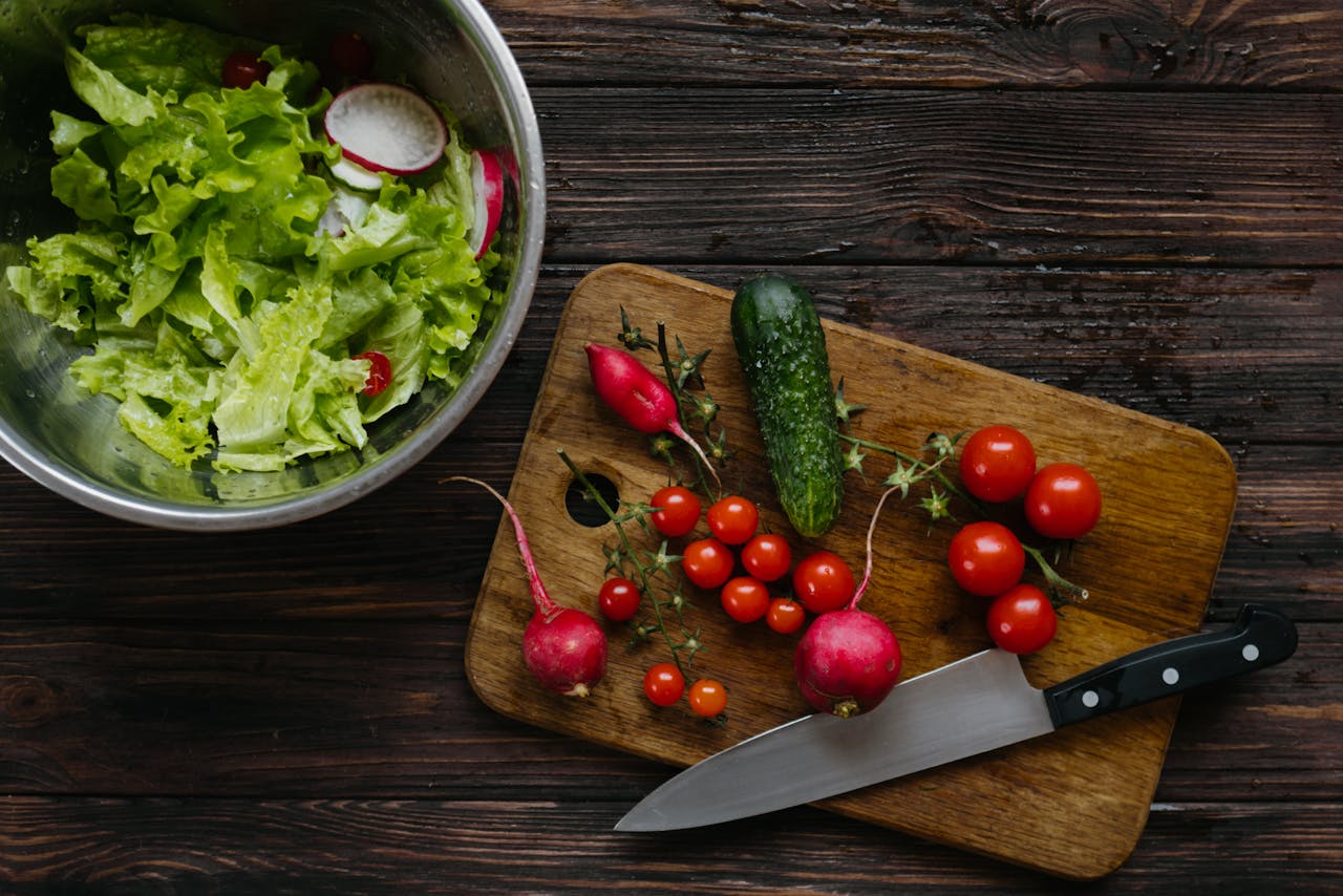 Top view of fresh salad ingredients including cherry tomatoes and radishes on a wooden board.